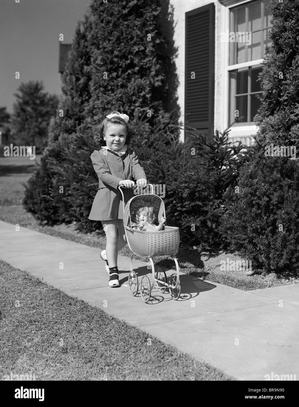 1940s LITTLE GIRL WALKING PUSHING STROLLER DOLL SIDEWALK Stock Photo