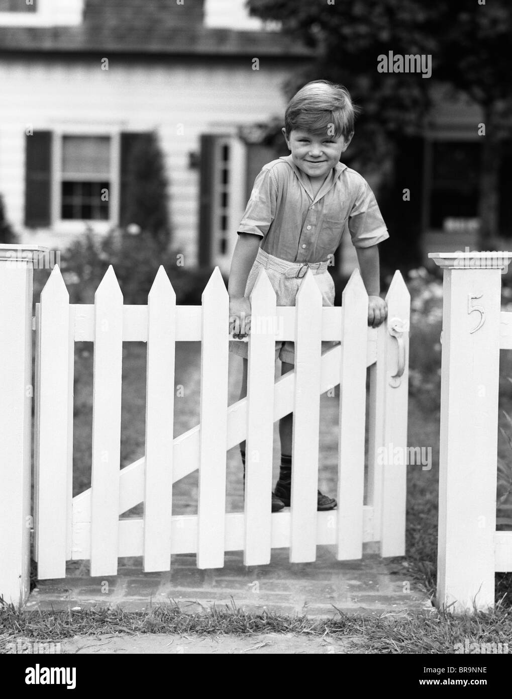 1940s CHILD STANDING ON FENCE SMILING LOOKING AT CAMERA Stock Photo
