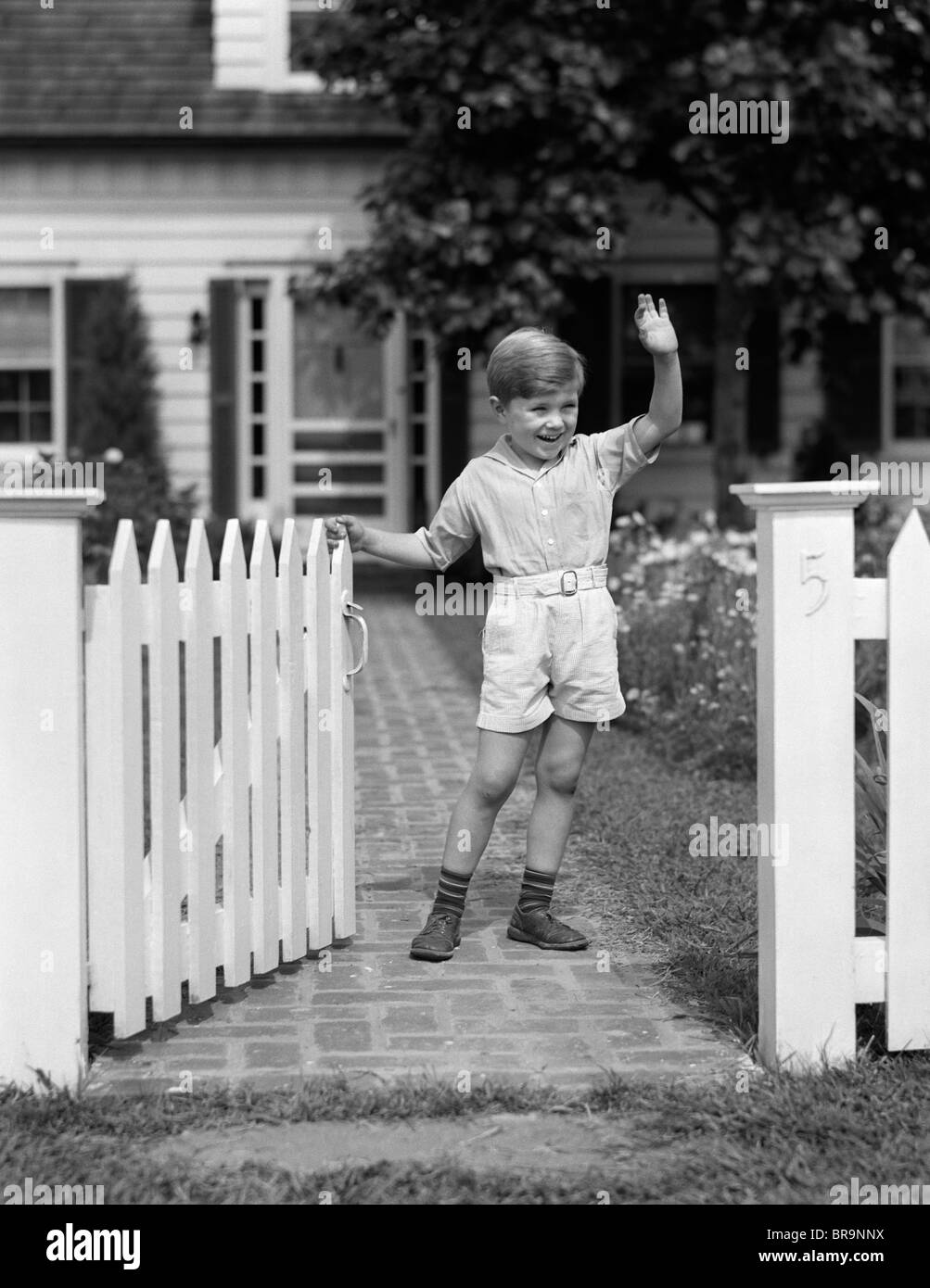 1940s BOY STANDING NEAR FENCE GATE WAVING Stock Photo