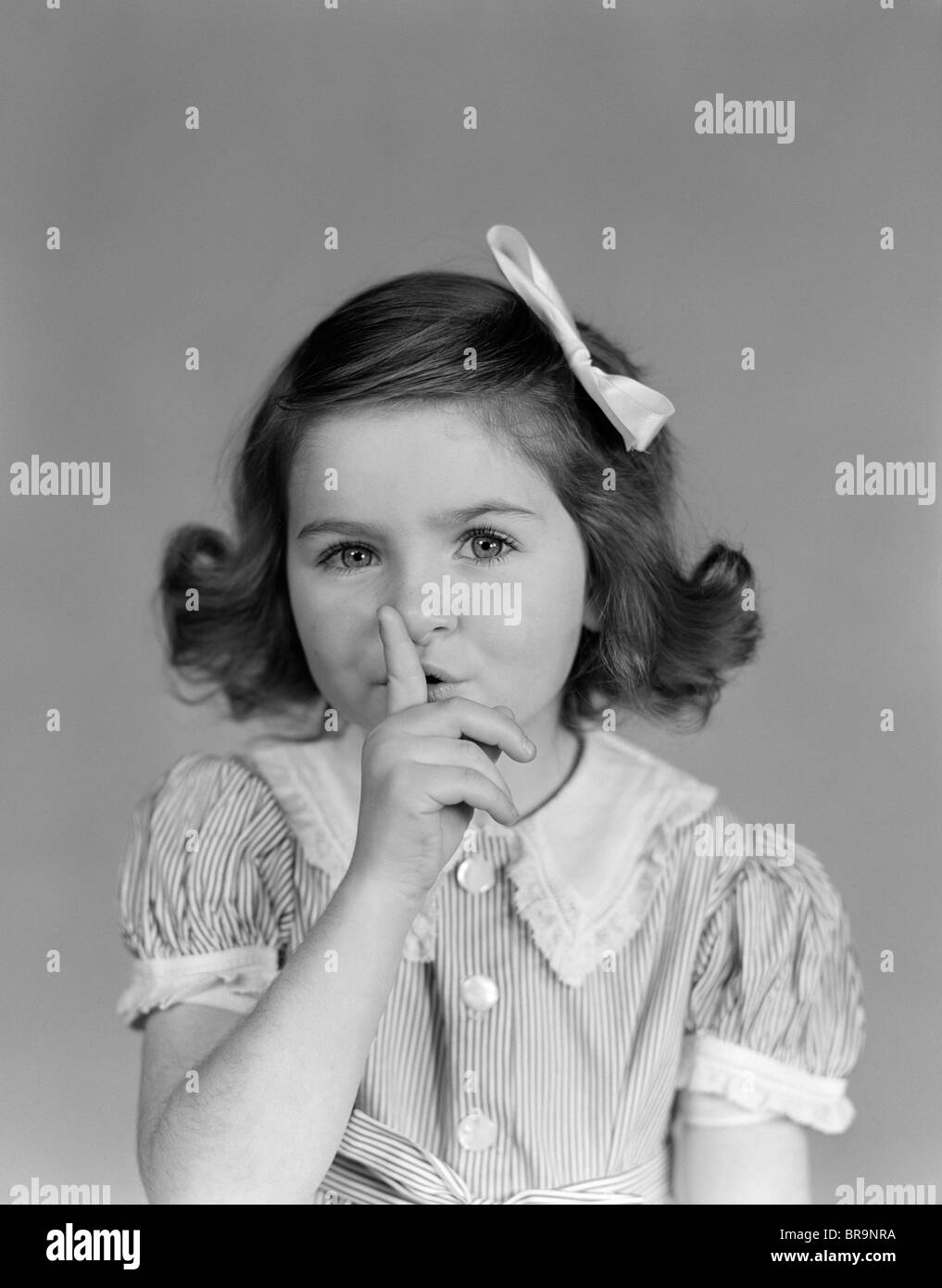 1940s LITTLE GIRL MAKING QUIET GESTURE FINGER ON LIPS LOOKING AT CAMERA Stock Photo