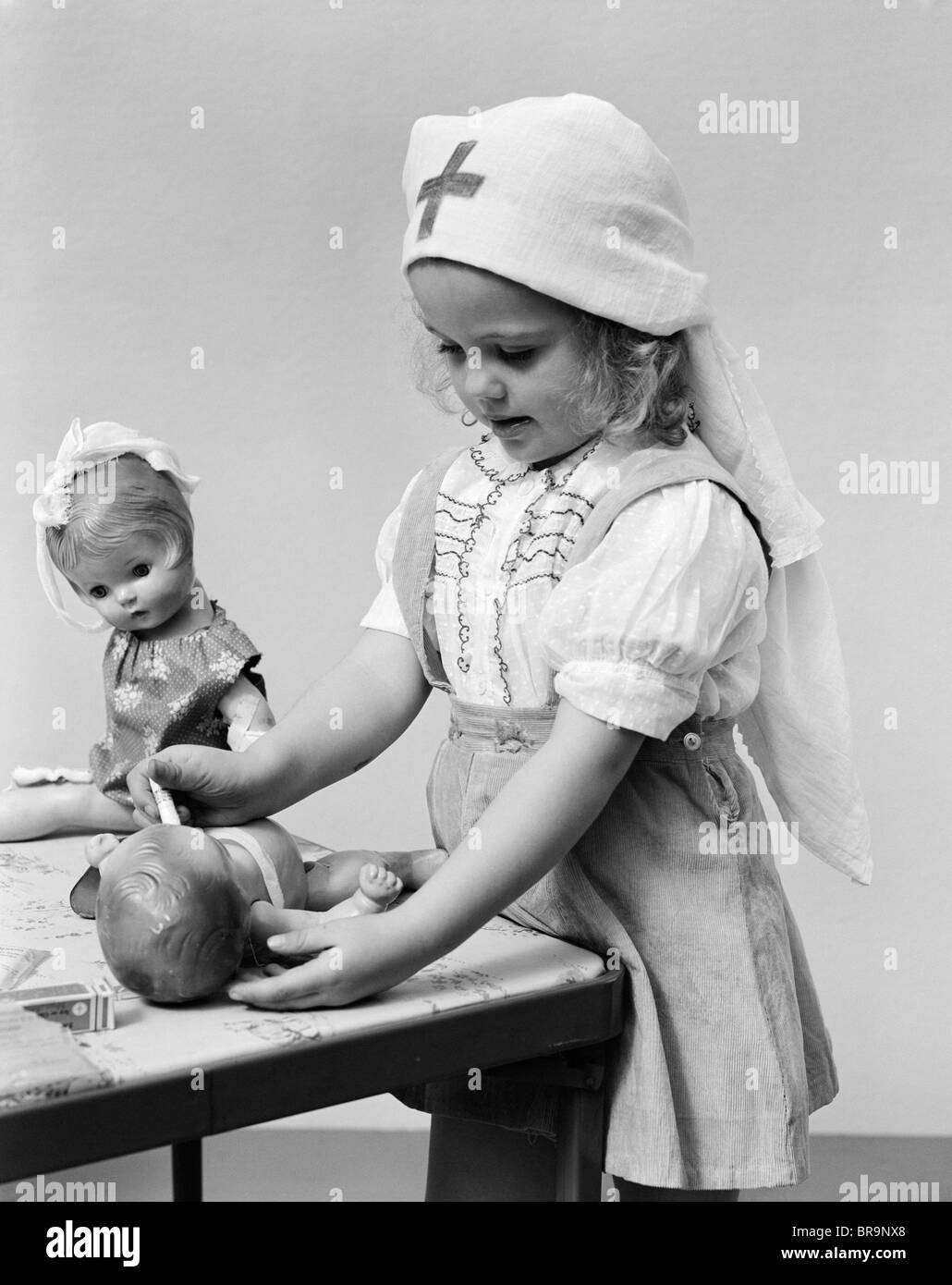 1940s CHILD PLAYING NURSE WITH DOLLS Stock Photo