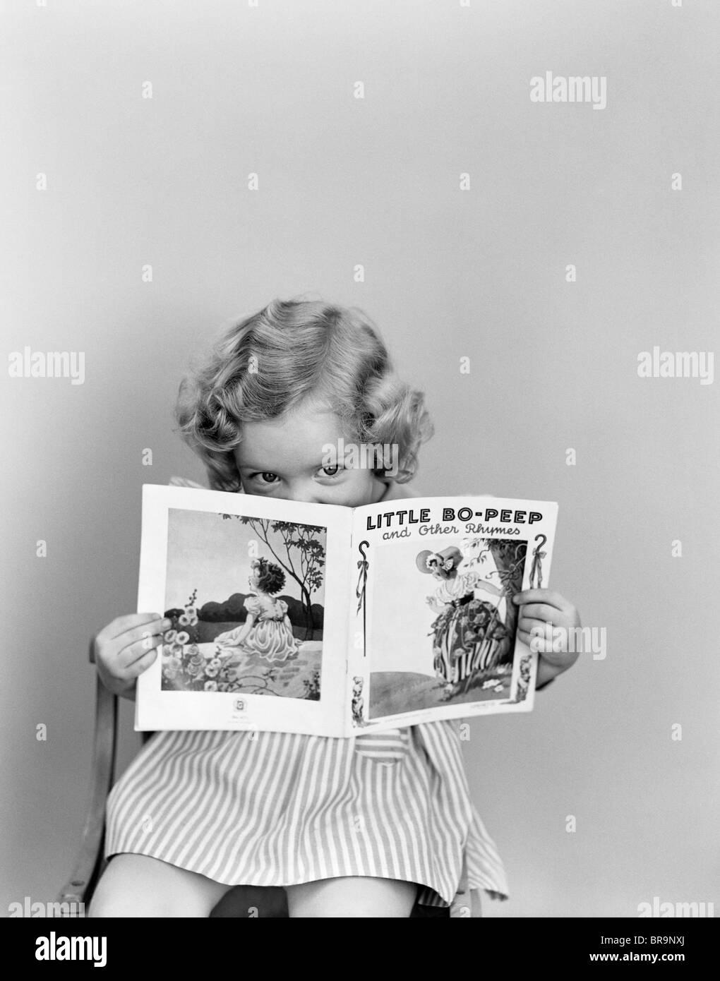 1940s LITTLE GIRL PEEKING OVER TOP OF LITTLE BO-PEEP NURSERY RHYME BOOK Stock Photo