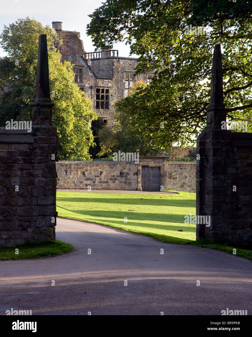 The ruined Hardwick Old Hall Derbyshire seen through the obelisk gate posts flanking the road Stock Photo