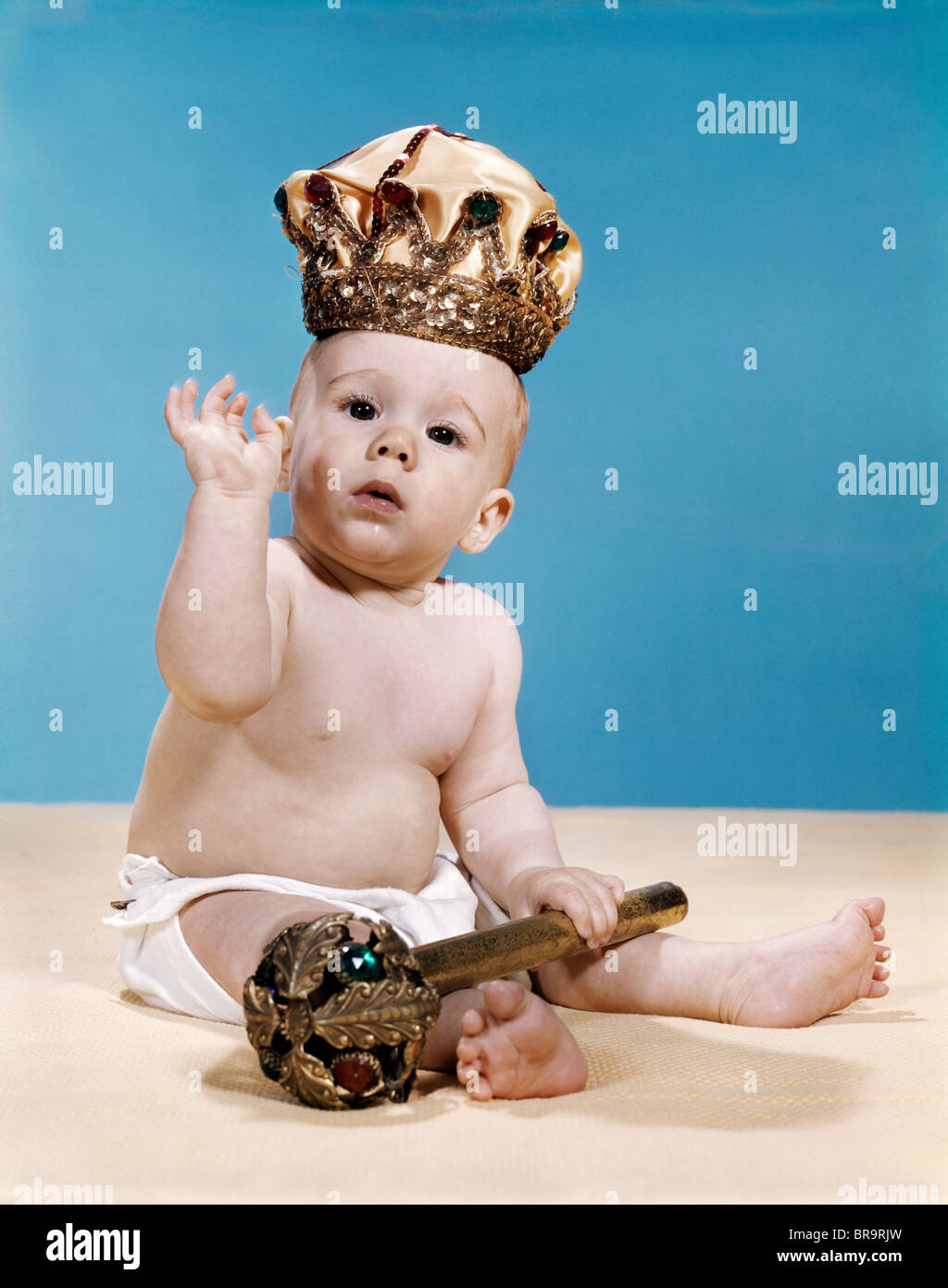 1960s BABY WEARING CLOTH DIAPER AND CROWN HOLDING A SCEPTER WAVING WITH ONE ARM RAISED LOOKING AT CAMERA Stock Photo