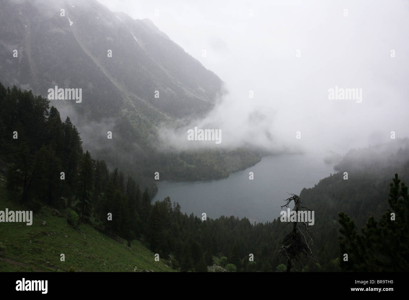 Rising mist and low cloud swirl over Sant Maurici lake on Pyrenean traverse and National Park Pyrenees Spain Stock Photo