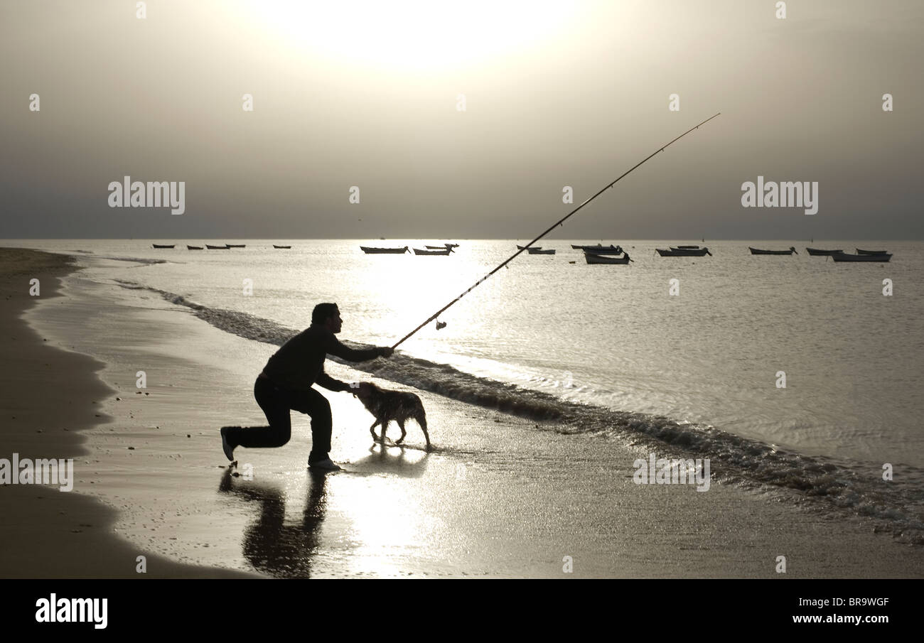 A man with his dog fishes at the mouth of the Gualdalquivir River Stock Photo