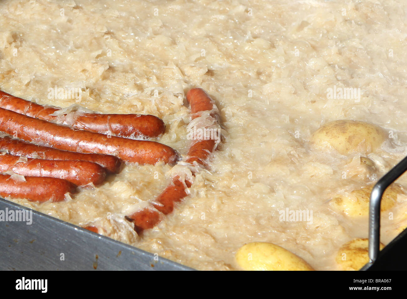 A large pan of potato rosti and bratwurst sausages cooking outside in Switzerland. This image was taken at the ski resort of Kle Stock Photo