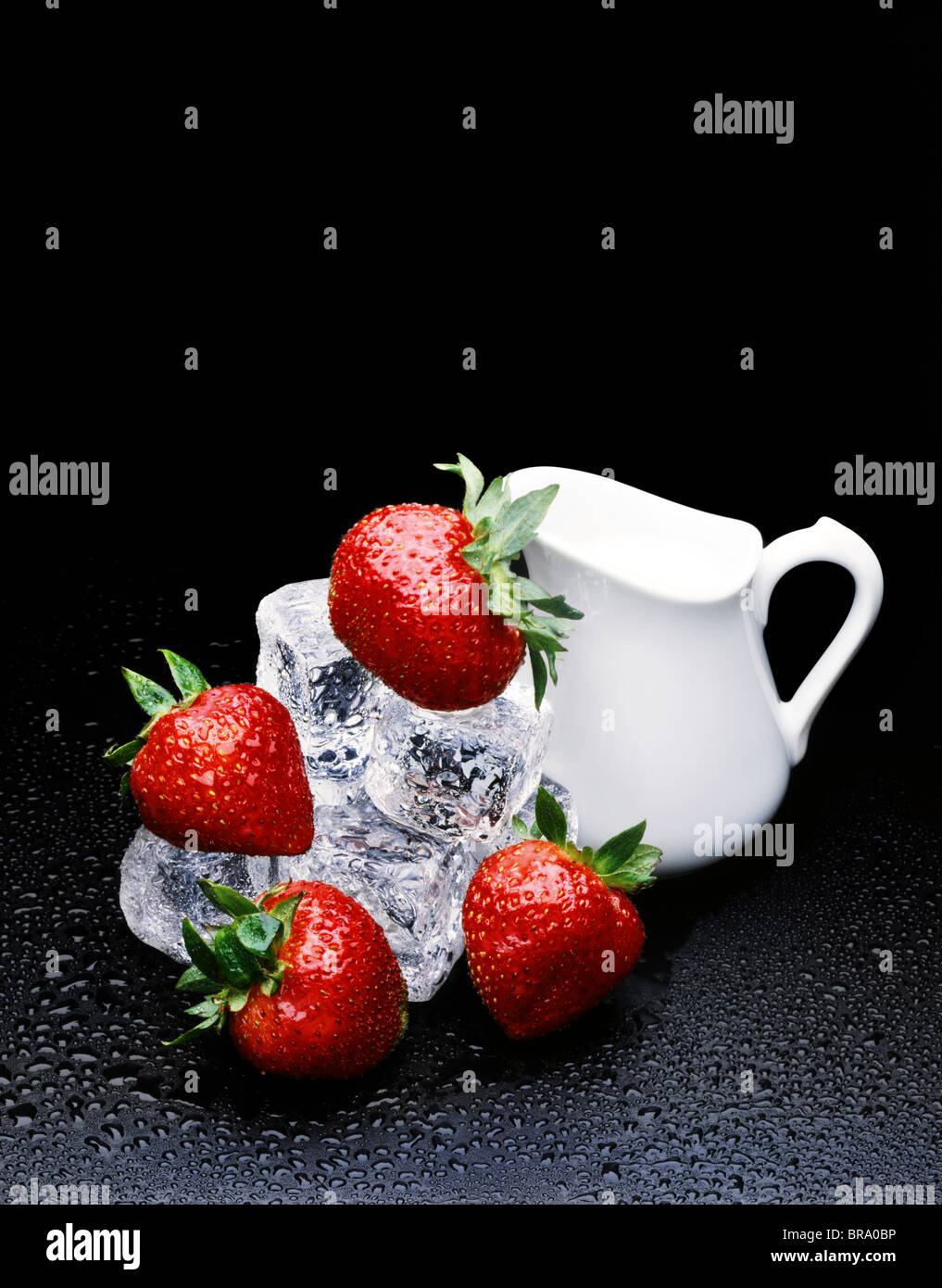 1980s STRAWBERRIES ON ICE WITH CREAM PITCHER BLACK BACKGROUND Stock Photo