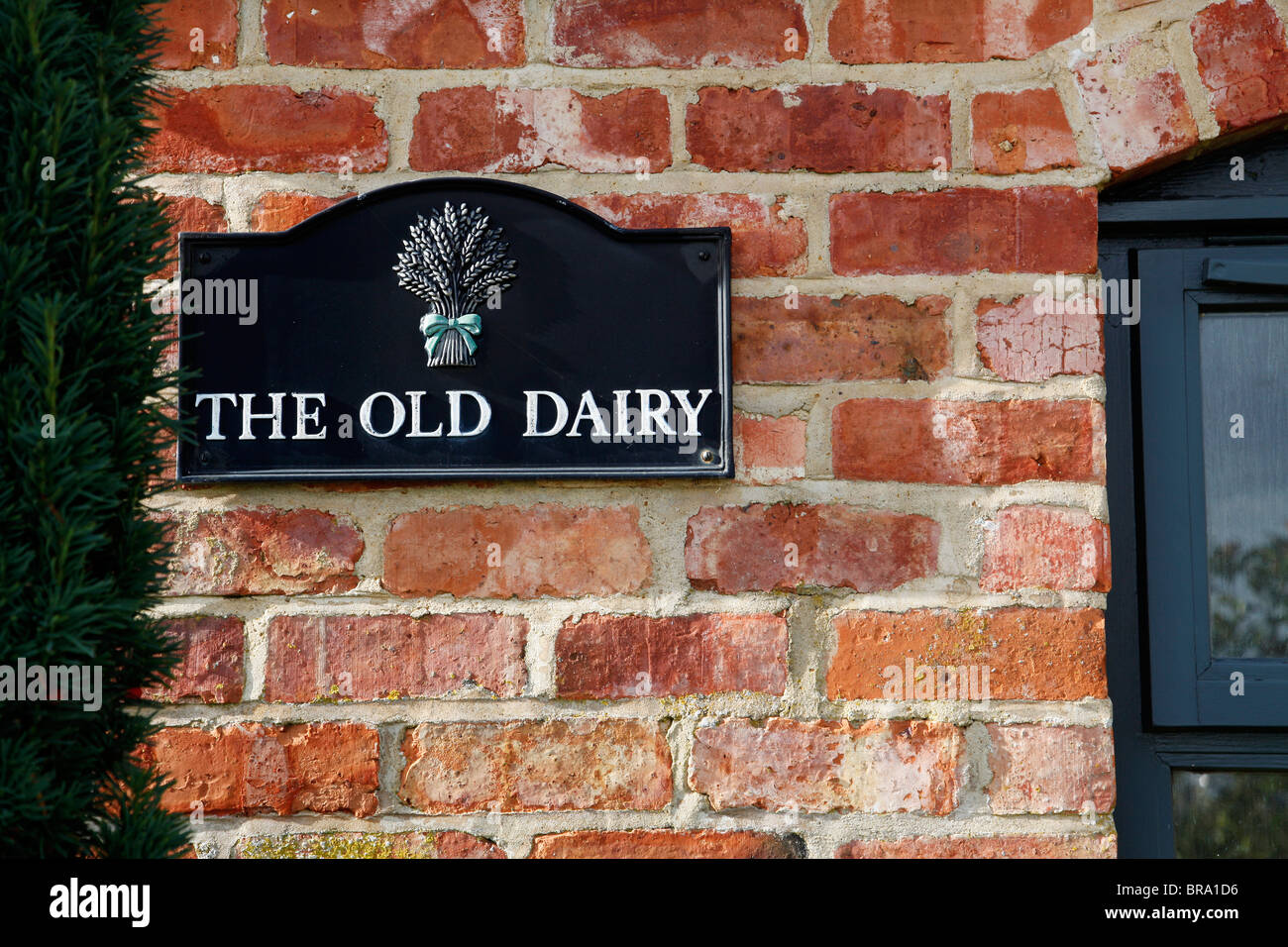 A traditional metal sign for The Old Dairy against a red brick wall Stock Photo