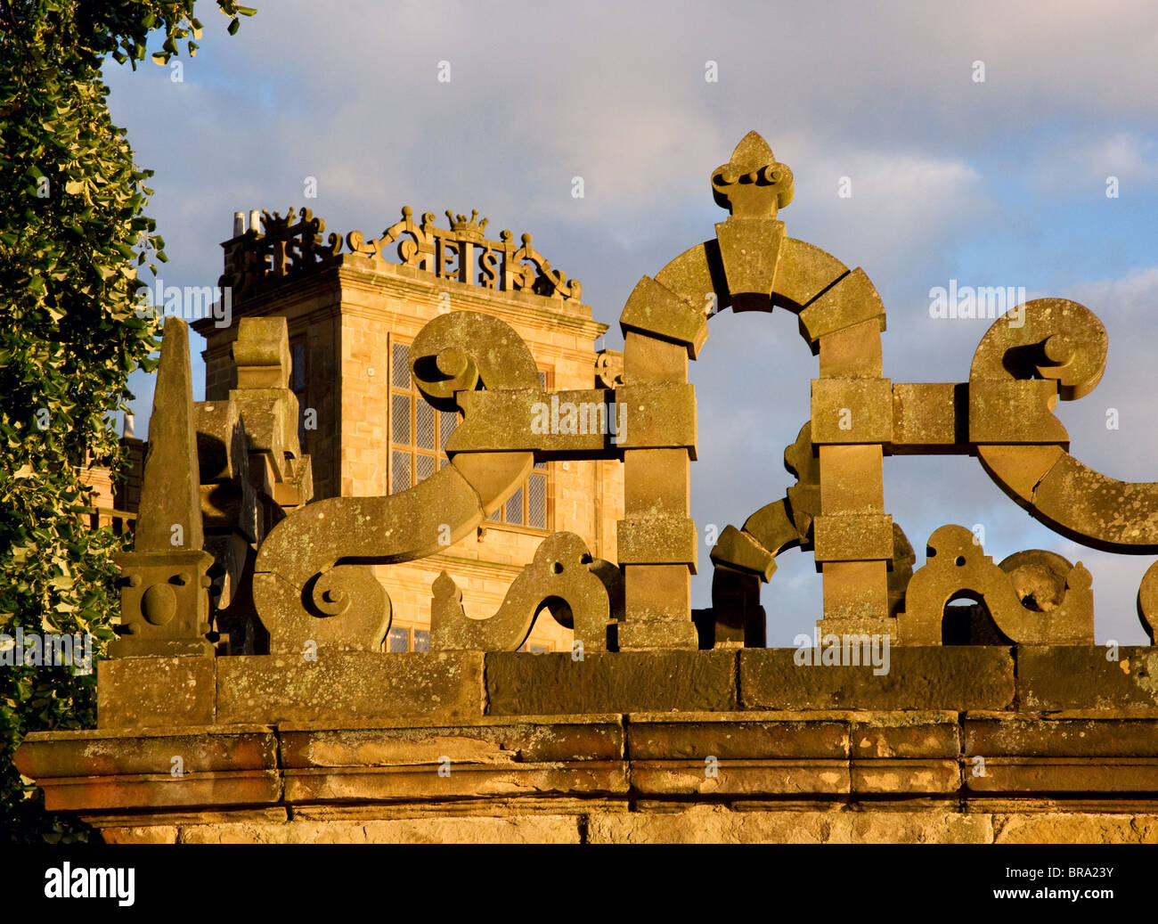 Evening sunlight casts a golden glow on the facade of Hardwick Hall in Derbyshire seen through stone strapwork of garden wall Stock Photo