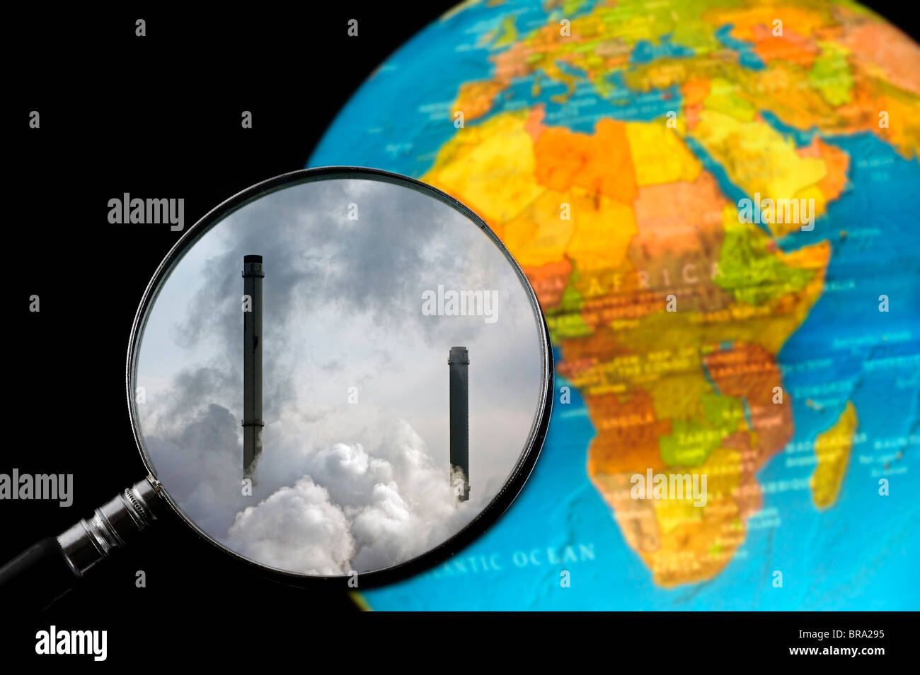 Chimneys covered in smoke seen through magnifying glass held against illuminated terrestrial globe Stock Photo