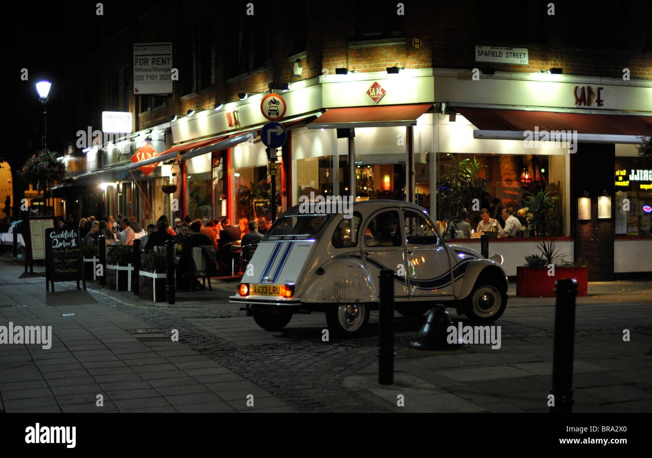 Citroen 2CV in Exmouth Market drives down past diners outside at night Stock Photo