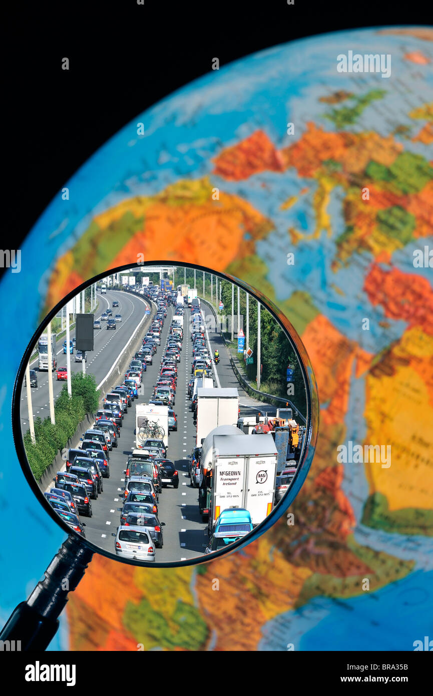 Cars in traffic jam on motorway during summer holidays seen through magnifying glass held against illuminated terrestrial globe Stock Photo