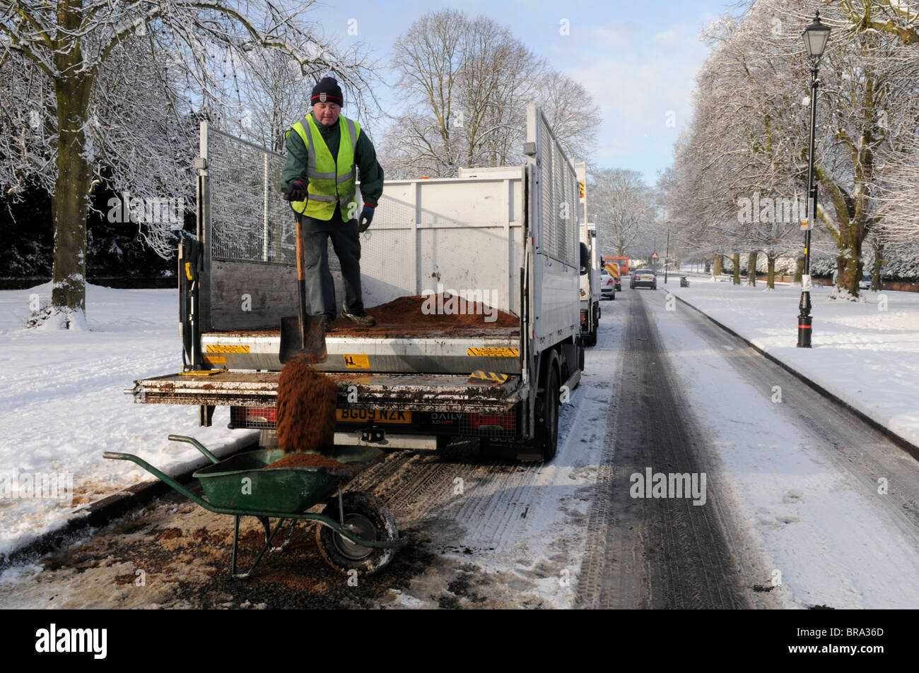 A workman shovels grit from the back of a lorry into a wheelbarrow on a snow-covered road in Tettenhall, Wolverhampton. Stock Photo