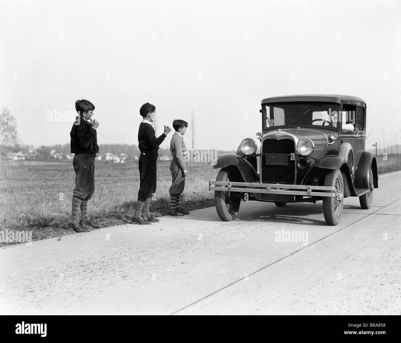 1930s 1920s MAN DRIVING FORD MODEL A CAR 3 BOYS HITCHHIKING Stock Photo
