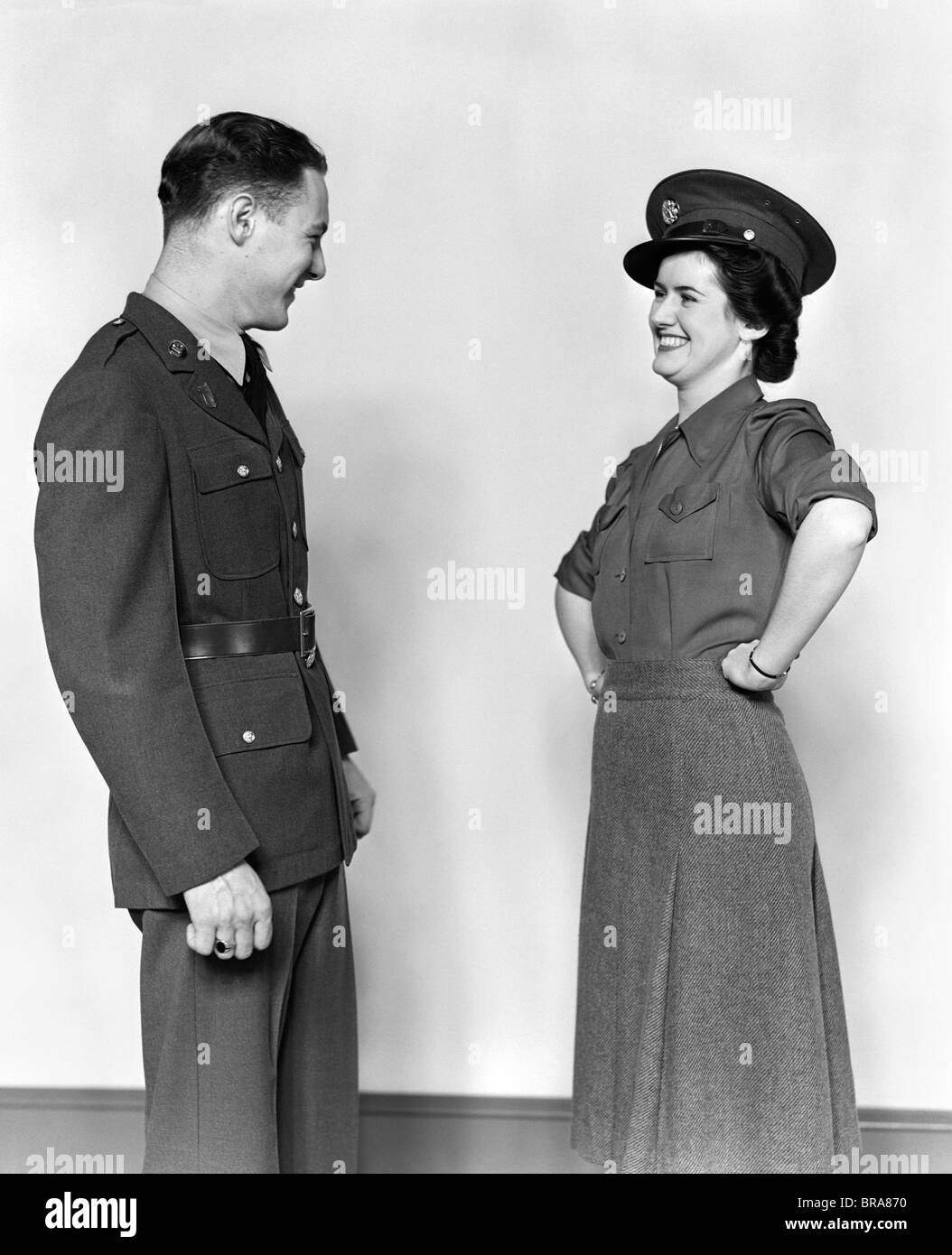 1940s COUPLE MAN IN UNIFORM WOMAN SMILING WEARING HIS HAT HANDS ON HIPS Stock Photo