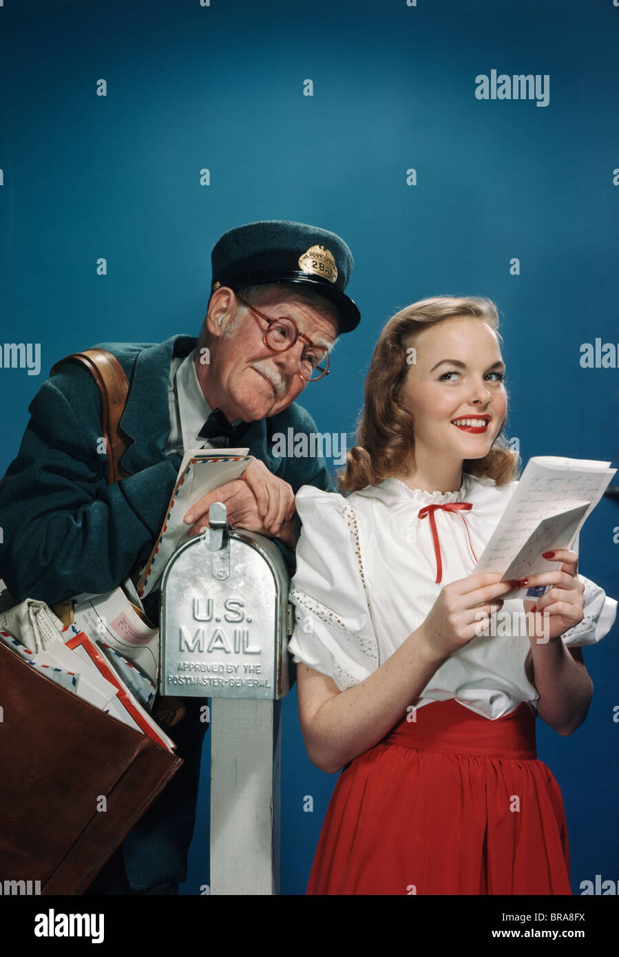 1940s 1950s ELDERLY MAILMAN READING OVER THE SHOULDER OF YOUNG WOMAN HOLDING LETTER Stock Photo