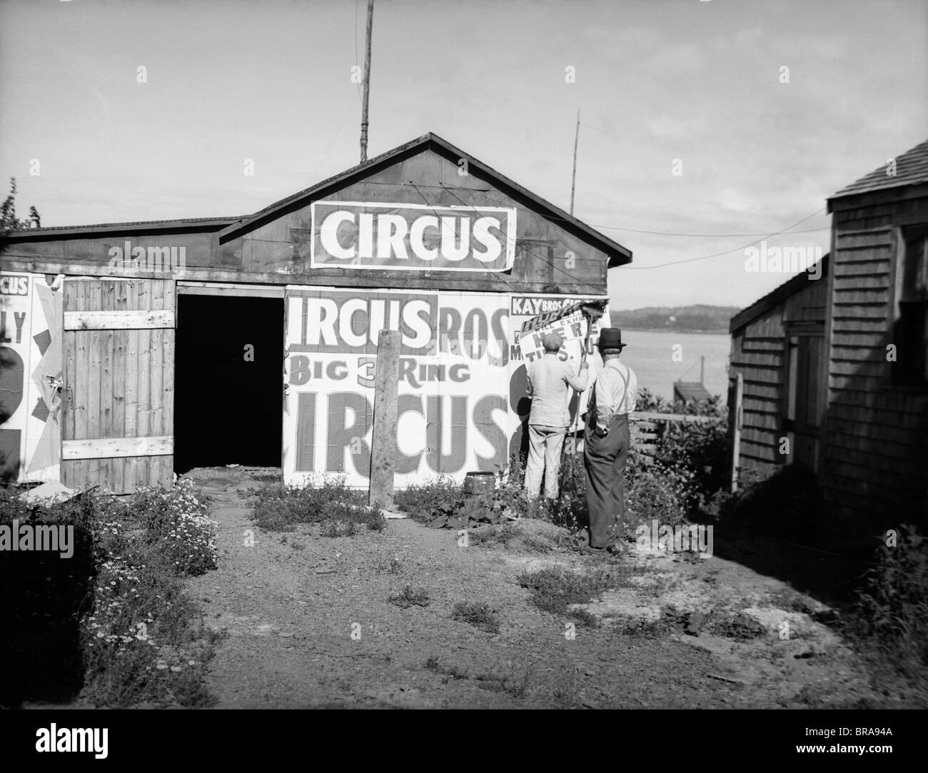 1920s BILL POSTERS STICKING SIGNS ON THE SIDE OF A BARN ADVERTISING A TRAVELING CIRCUS Stock Photo