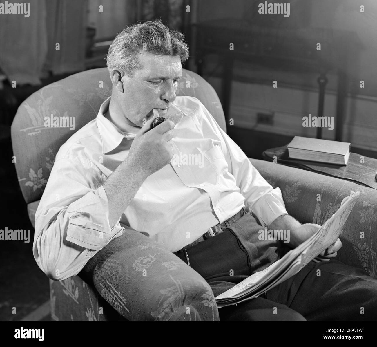 1930s MAN SITTING CHAIR READING NEWSPAPER SMOKING PIPE Stock Photo