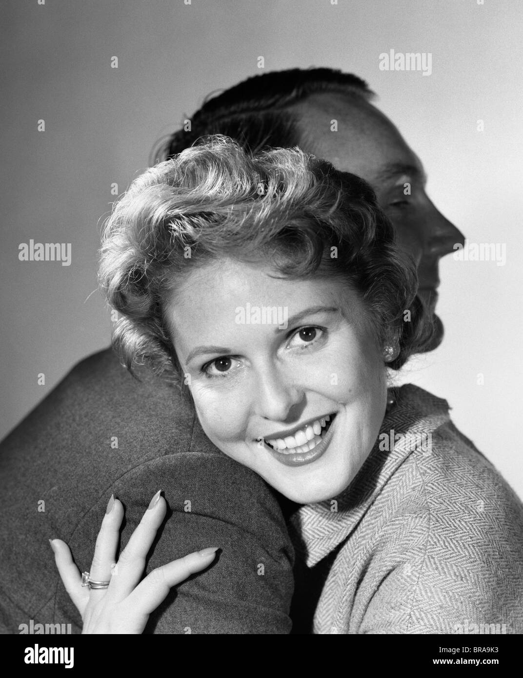 1950s SMILING WOMAN HUGGING MAN HEAD ON HIS SHOULDER LOOKING AT CAMERA Stock Photo