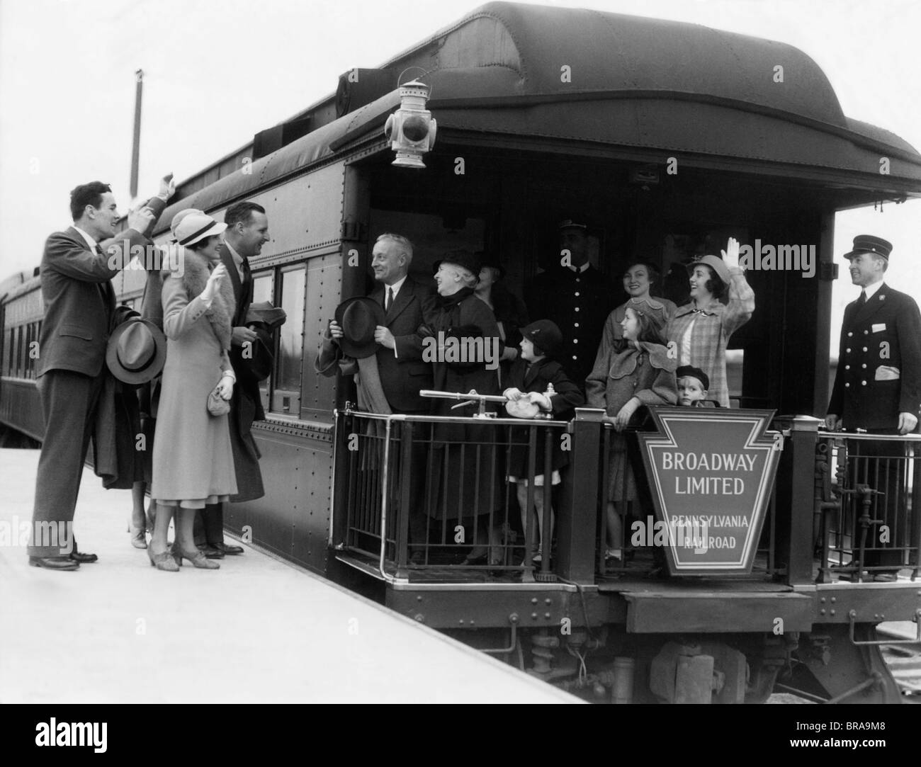 1930s FAMILY WITH GRANDPARENTS & CONDUCTOR ON BROADWAY LIMITED OBSERVATION CAR TRAIN PLATFORM WAVING GOODBYE & FAREWELL Stock Photo