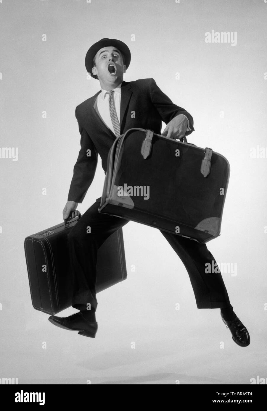 1960s MAN SALESMAN BUSINESSMAN WITH TWO SUITCASES RUNNING JUMPING EXCITED LOOKING AT CAMERA Stock Photo