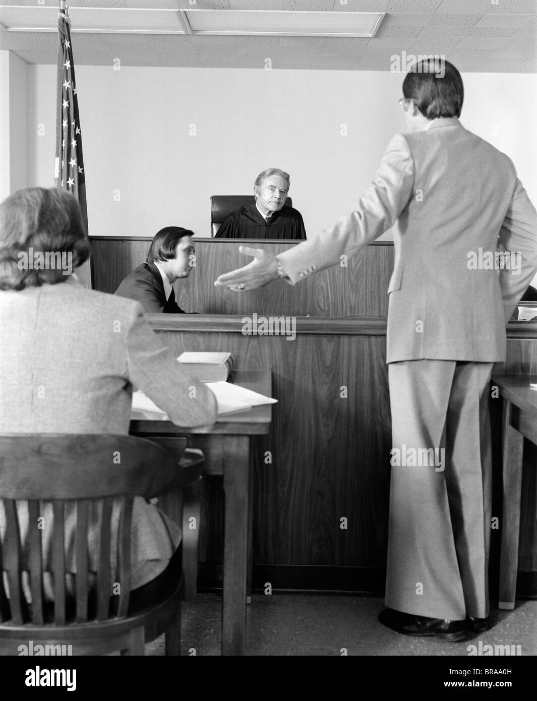 1970s LAWYER POINTING TO PLAINTIFF PLEADING CASE BEFORE COURT ROOM JUDGE Stock Photo