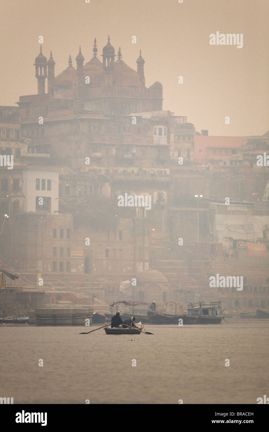 A boat is rowed on a typically foggy morning in the Ganga (Ganges) River at Varanasi, Uttar Pradesh, India, Asia Stock Photo