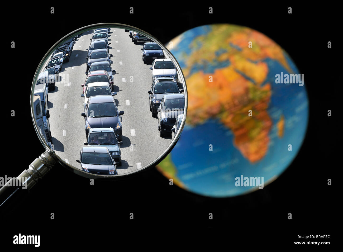 Cars in traffic jam on motorway during summer holidays seen through magnifying glass held against illuminated terrestrial globe Stock Photo