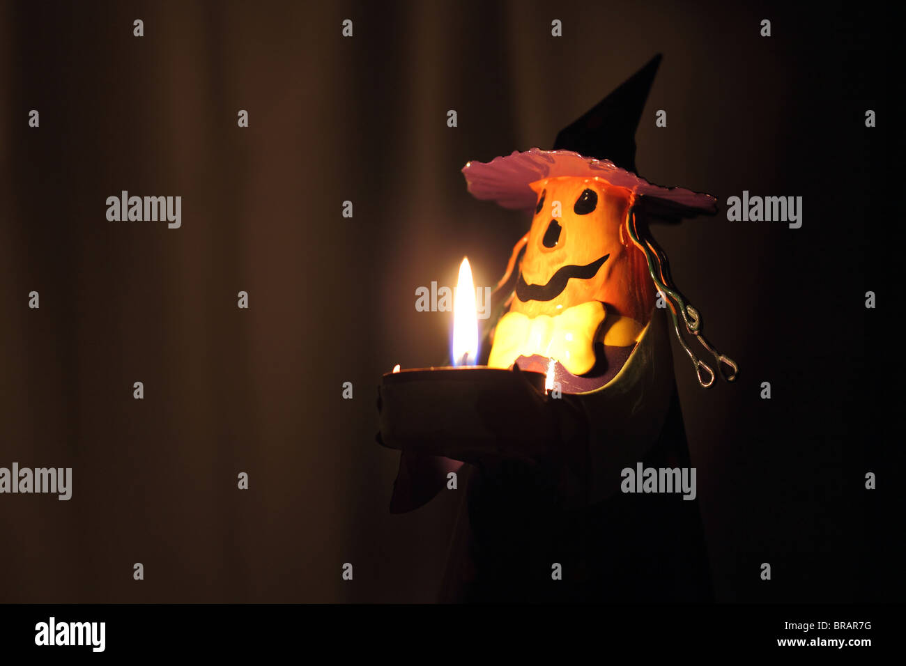 A Halloween decoration that has the face of a Jack-o-Lantern and the pointy hat of a witch. Shot in the dark, only light source is a candle. Stock Photo
