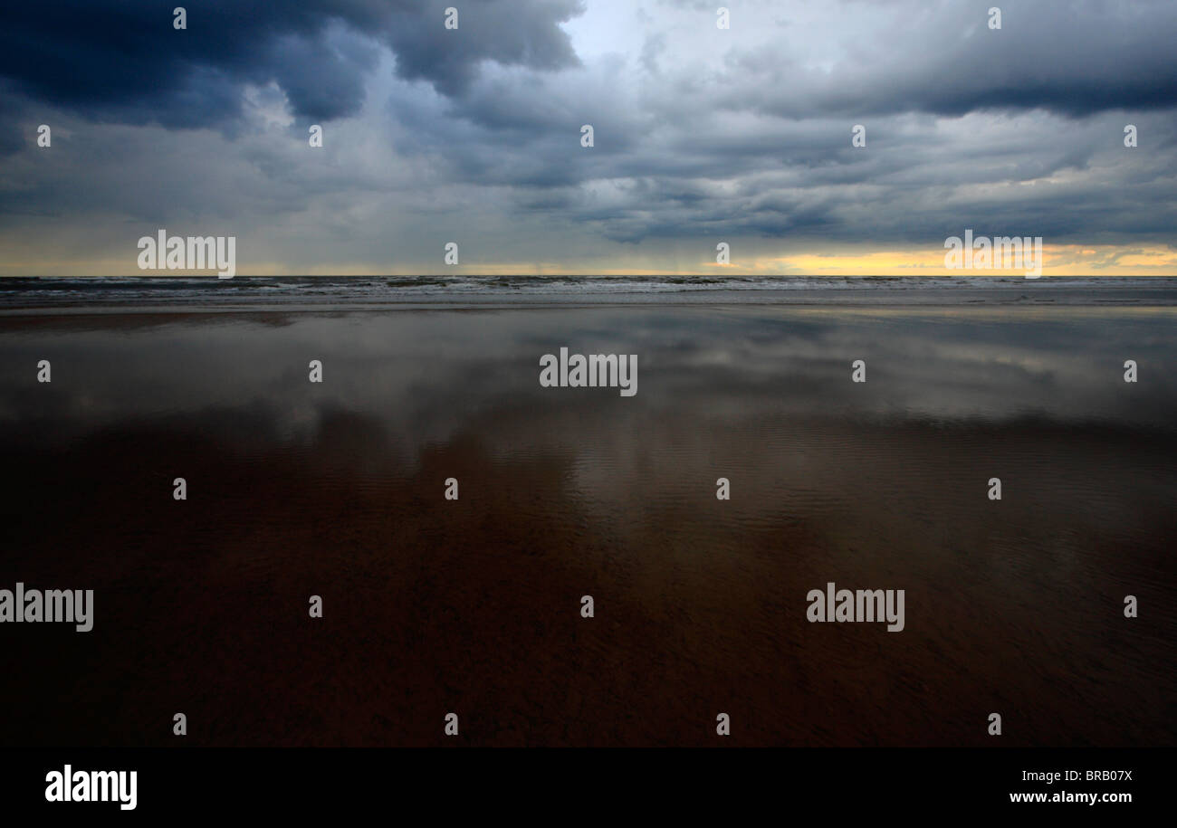 Strormy clouds reflected on wet sand on the Norfolk coast. Stock Photo