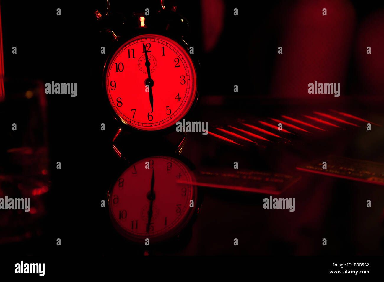 Alarm Clock, strip cocaine and credit cards on glass table at a red light Stock Photo