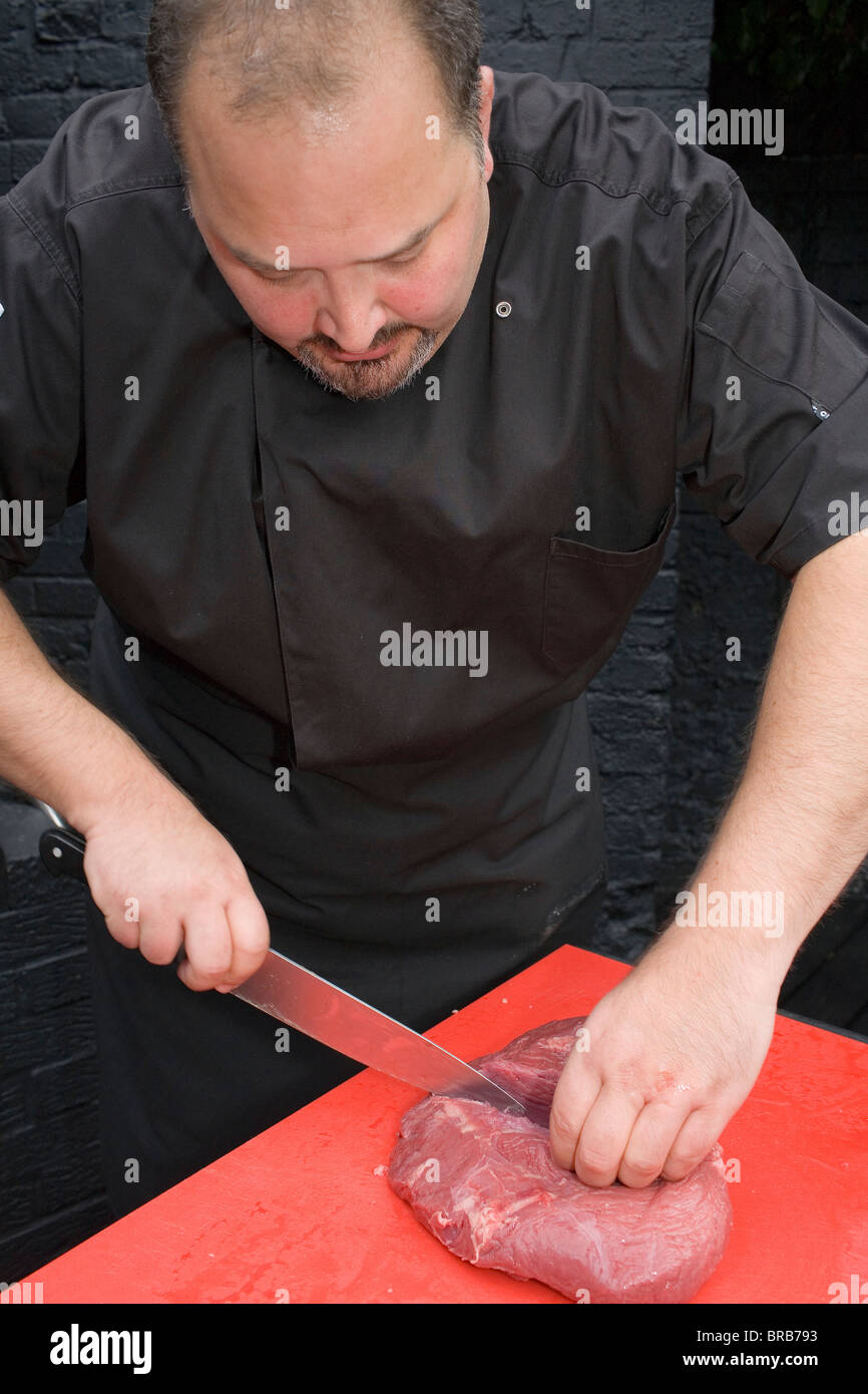 https://c8.alamy.com/comp/BRB793/a-man-cutting-a-piece-of-beef-on-a-red-chopping-board-with-a-large-BRB793.jpg
