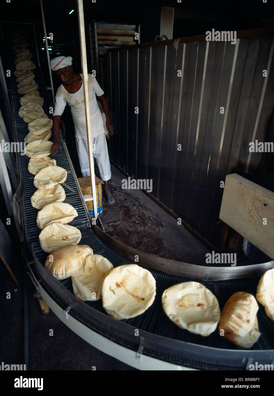 Qatar Doha Male Baker In Bakery Standing Beside Conveyor Belt Carrying