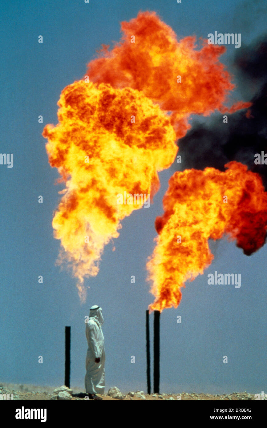 Saudi Arabia Middle East Gulf State Arab man standing beside pipes burning off gas at oil well Stock Photo