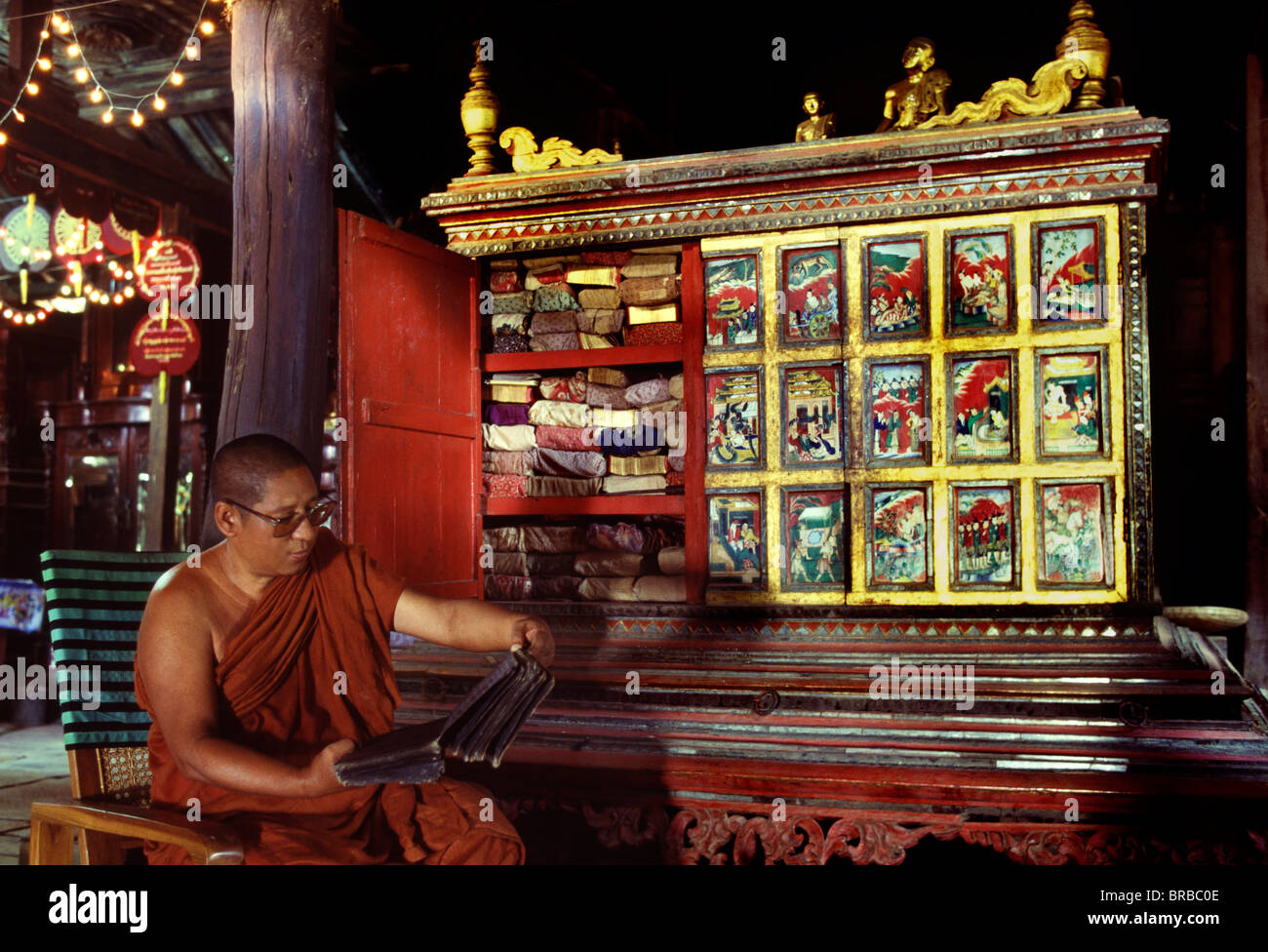 Monk reading a manuscript next to a manuscript cabinet, Mandalay, Myanmar (Burma) Stock Photo