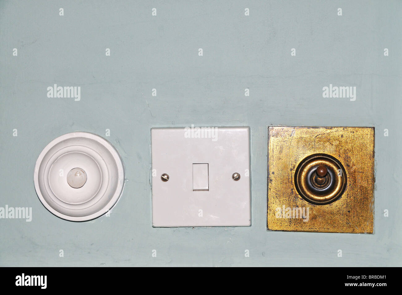 Old brass  and new plastic light switches and room  service bell positioned in a row on a room wall. Stock Photo
