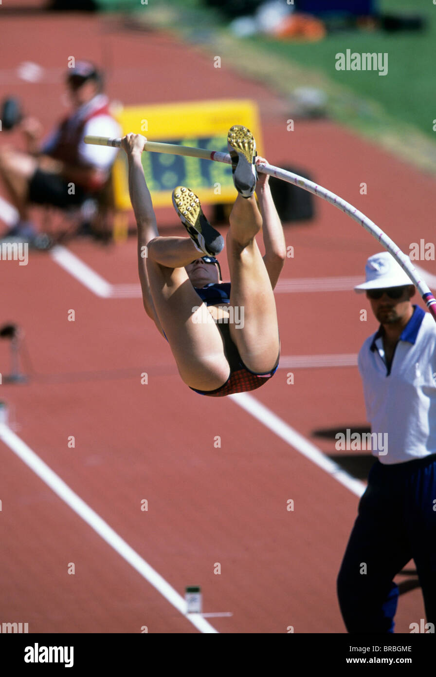 Female pole vaulter bends bar as she attempts a clearance watched closely by judge at track ...