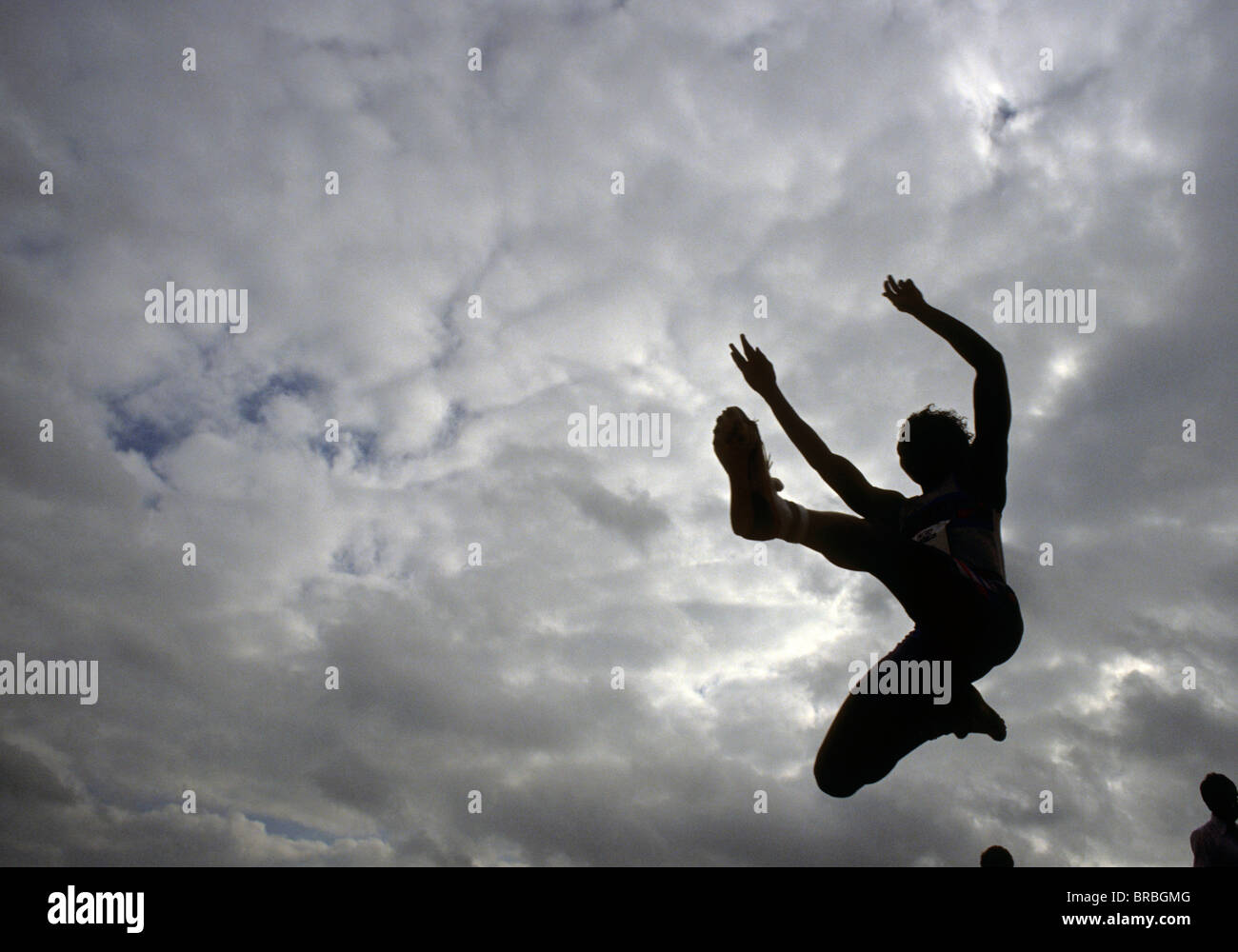 Female long jumper seen from below against stormy skies Stock Photo