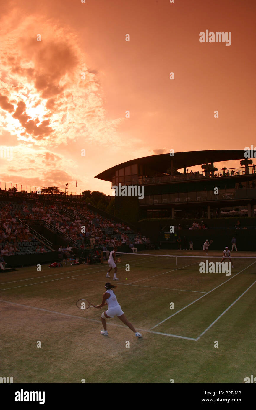 Doubles match on a grass tennis court against a setting sun Stock Photo