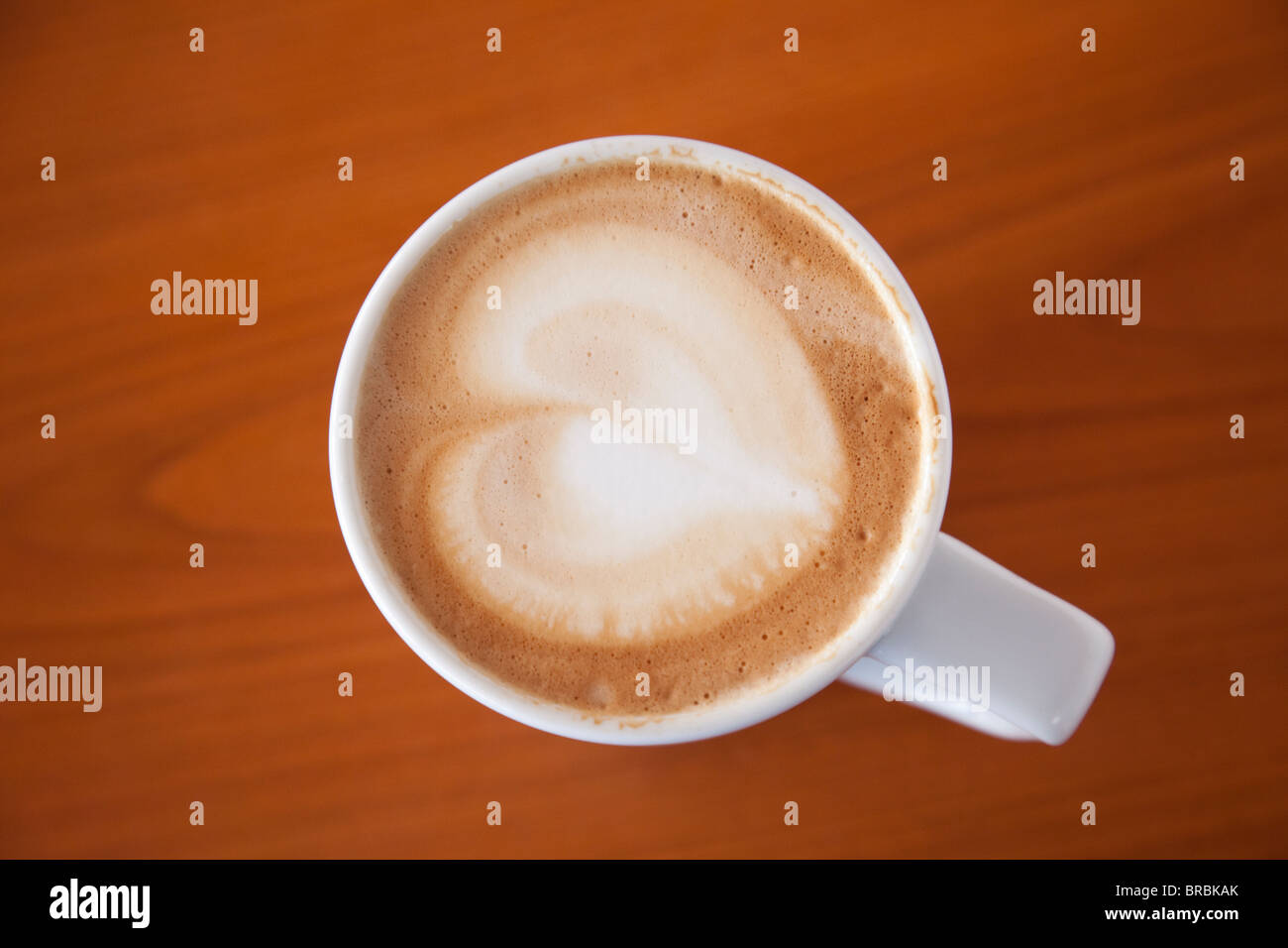 Top down of a mug of cafe Latte coffee with a heart shape in froth on top of a wooden table background from above. Love coffee concept Stock Photo