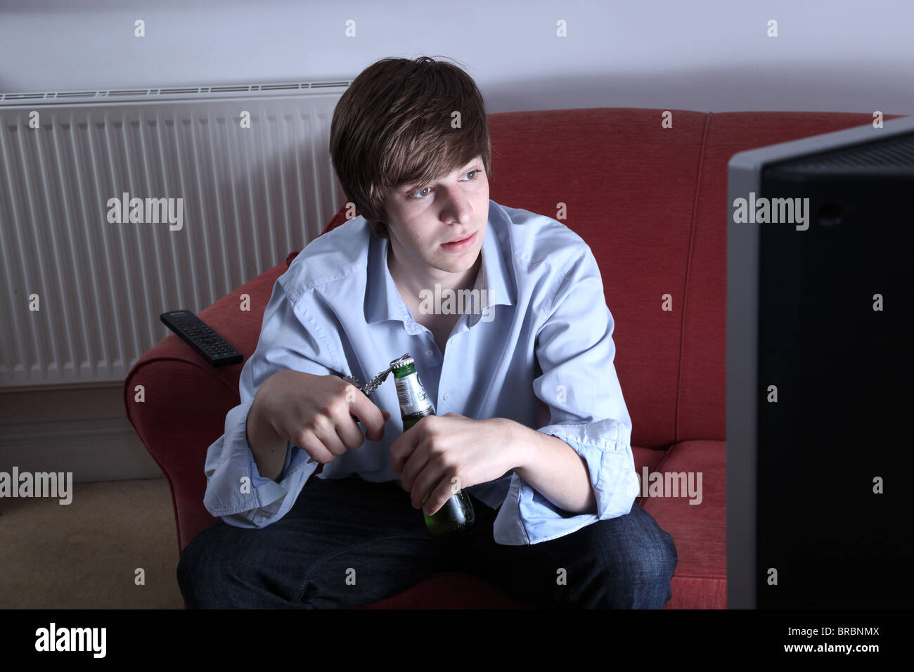 Young man alone watching tv while opening a bottle of beer Stock Photo