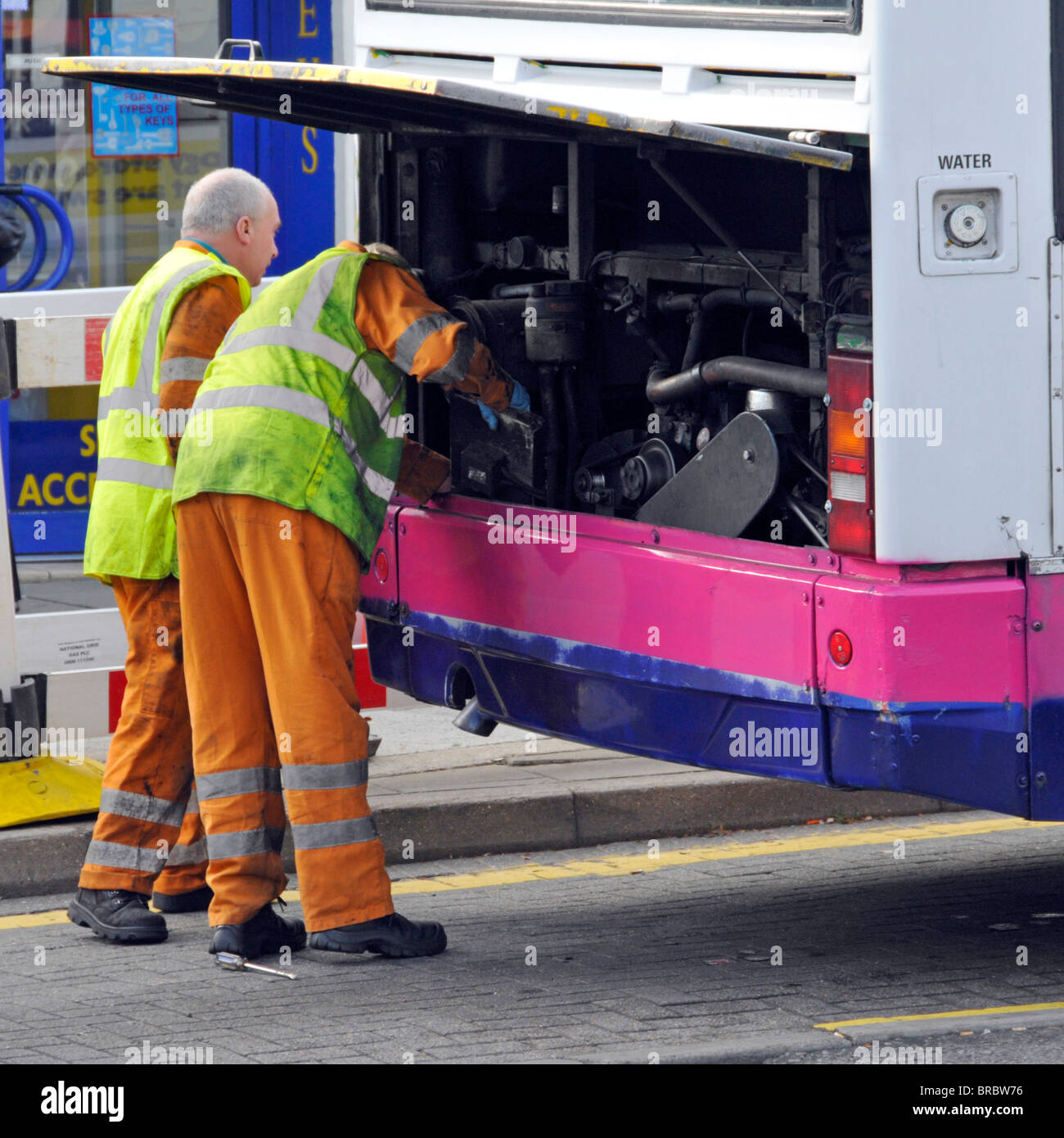 Mechanics examining engine compartment of broken down bus Stock Photo