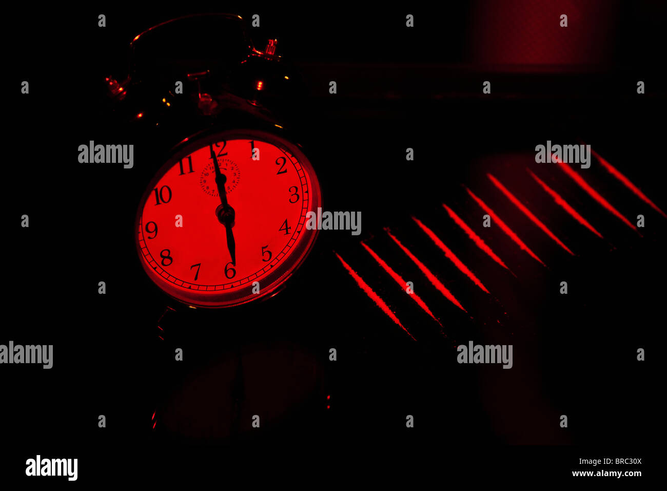 Alarm Clock and strip cocaine on glass table at a red light Stock Photo