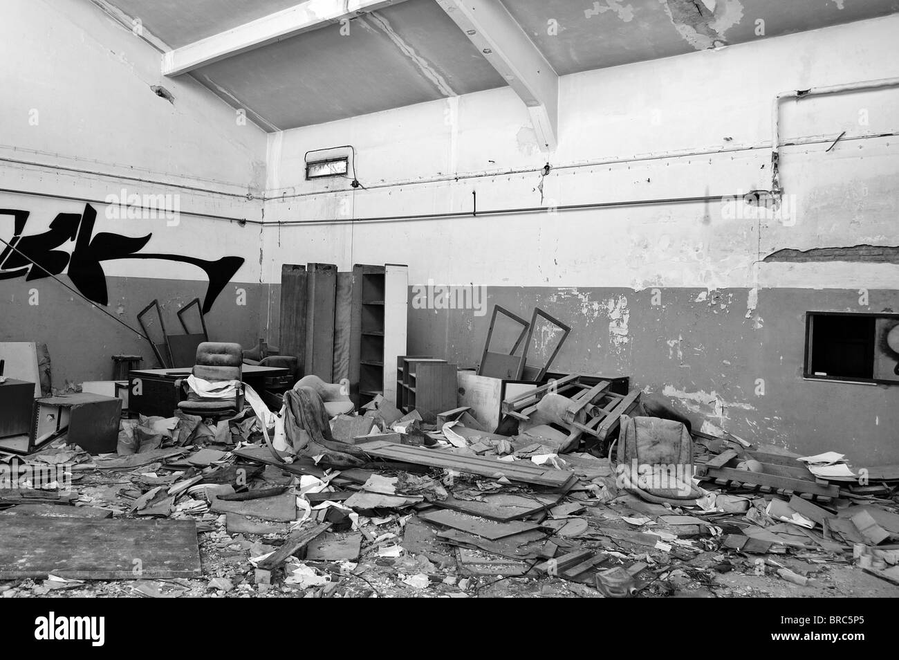 Vandalized equipment and debris in derelict factory. Black and white. Stock Photo