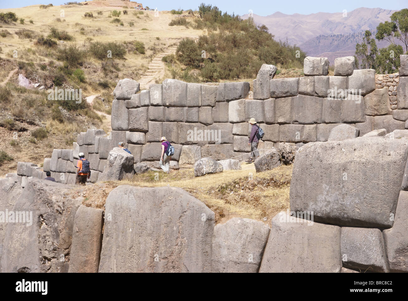 Tourists walking past massive stones in Inca fortress walls, Sacsayhuaman, Cusco, Peru, South America  Stock Photo
