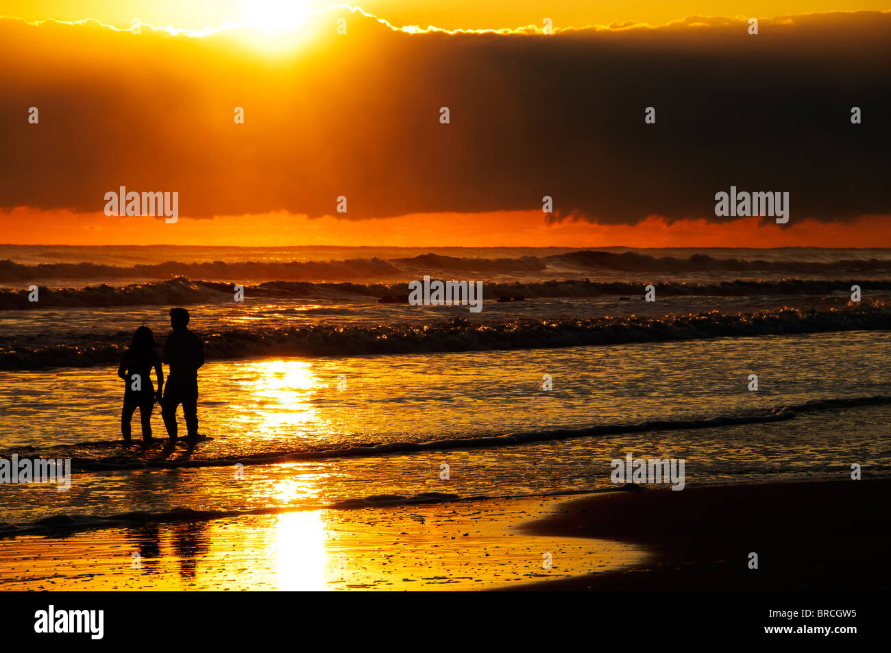 The silhouettes of a young couple enjoying the sunrise at the beach ...