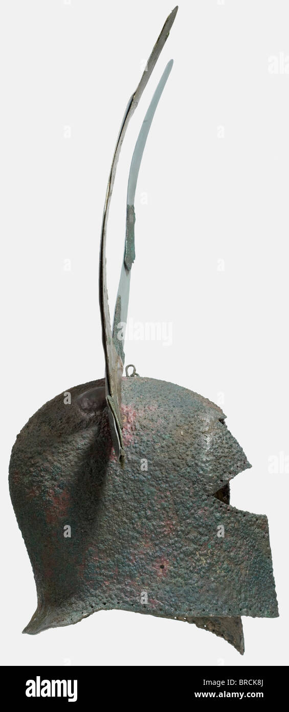 A Corinthian helmet with decorative horns, 7th - 6th century B.C. Bronze, heavy, tall archaic helmet with a strong nasal and large face cutout. Surmounted by a heavy detachable helmet adornment on, cut from sheet bronze in the shape of a bull's horns with large ears sticking out, and decorated on the front with wavy lines (right horn completely preserved). Profiled rails riveted to the base of the horns, which were formerly inserted into fittings on the helmet, now lost. Two transverse loops on the crown, and various holes in the walls of the helmet, a row of l, Stock Photo