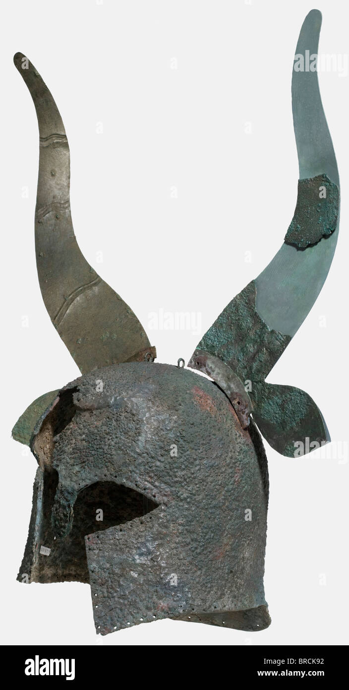 A Corinthian helmet with decorative horns, 7th - 6th century B.C. Bronze, heavy, tall archaic helmet with a strong nasal and large face cutout. Surmounted by a heavy detachable helmet adornment on, cut from sheet bronze in the shape of a bull's horns with large ears sticking out, and decorated on the front with wavy lines (right horn completely preserved). Profiled rails riveted to the base of the horns, which were formerly inserted into fittings on the helmet, now lost. Two transverse loops on the crown, and various holes in the walls of the helmet, a row of l, Stock Photo