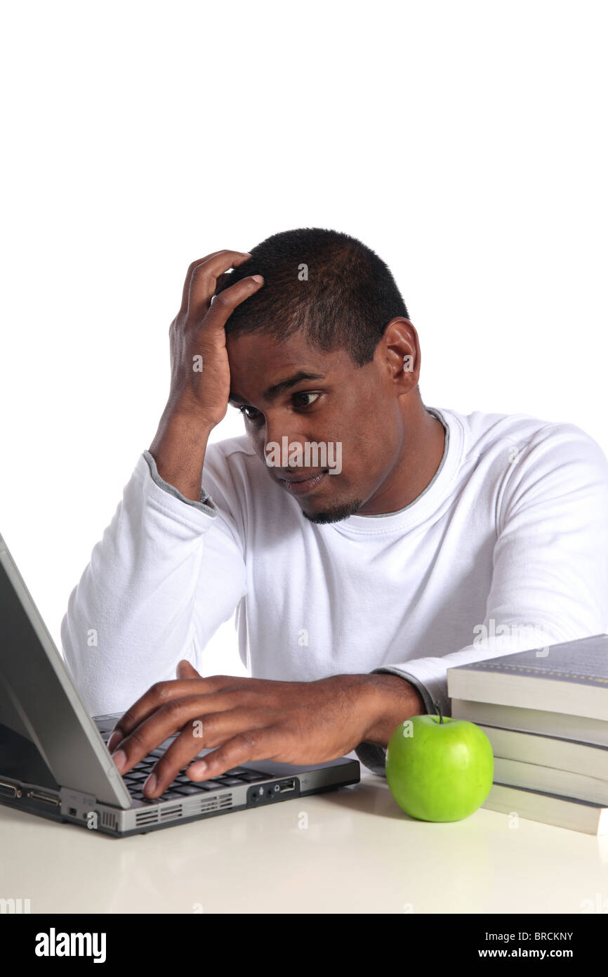 An attractive dark-skinned student in bad mood sitting in front of his notebook computer. All on white background. Stock Photo